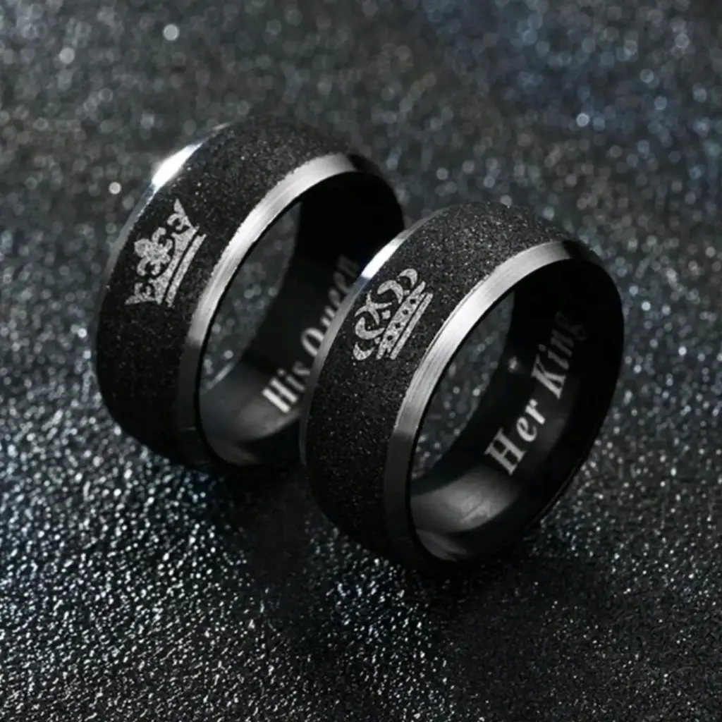 Set de dos anillos plateados con linea negra texturizada en el centro, con el grabado de "His Queen" y "Her King" dentro del anillo.